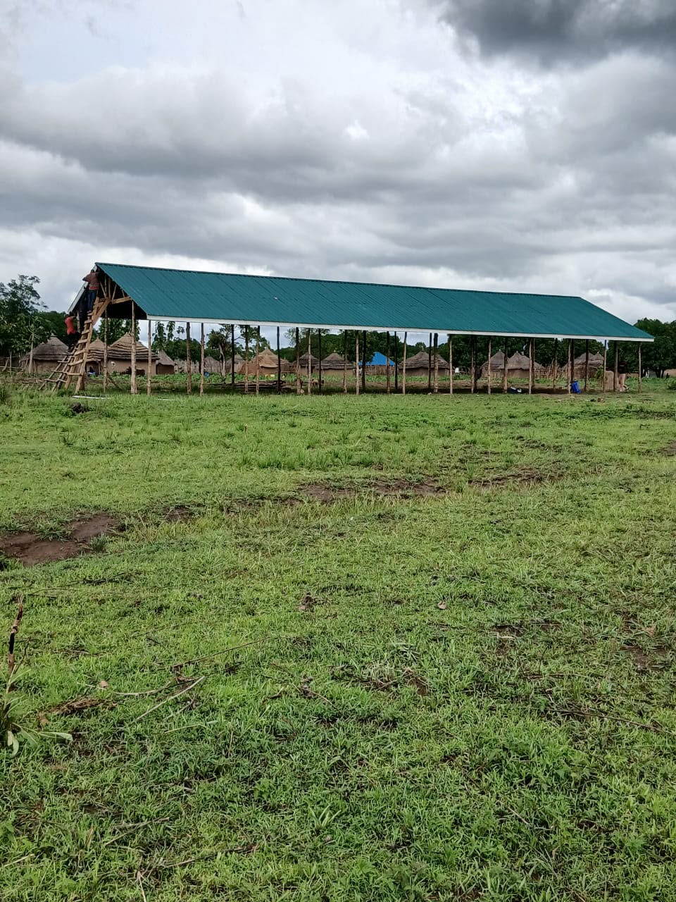 The long classroom block with green roofing sheets installed, seen from the school grounds.
